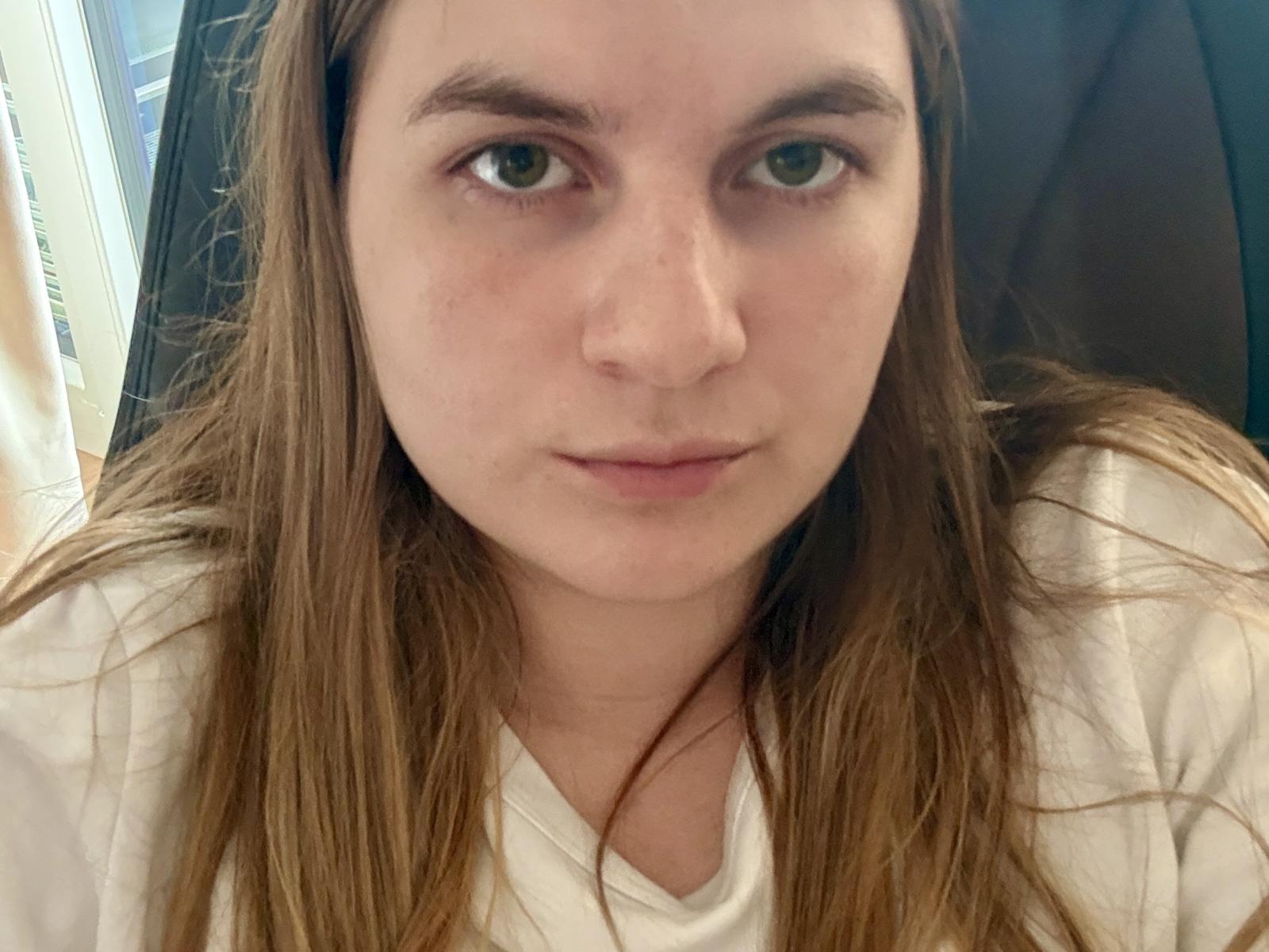 Bessie Jellinek ha lunghi capelli castani, occhi verdi e un viso leggermente lentigginoso, indossa una camicia bianca e guarda direttamente nella fotocamera con un'espressione neutra..