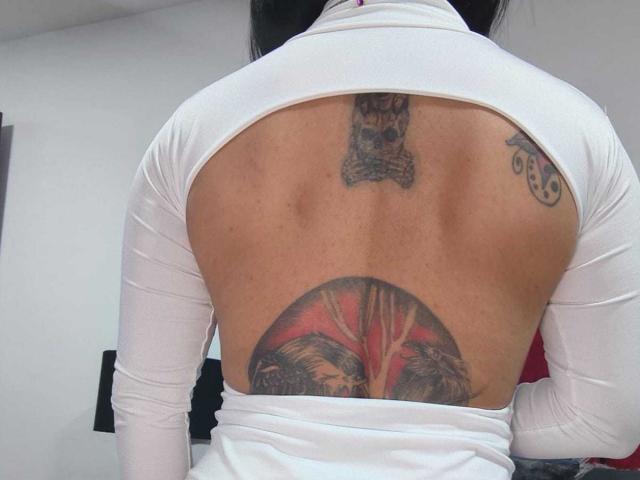 As costas de Amelie Blake têm três tatuagens: um crânio no centro superior, um desenho circular vermelho e preto na parte inferior e um pequeno espiral no lado direito..