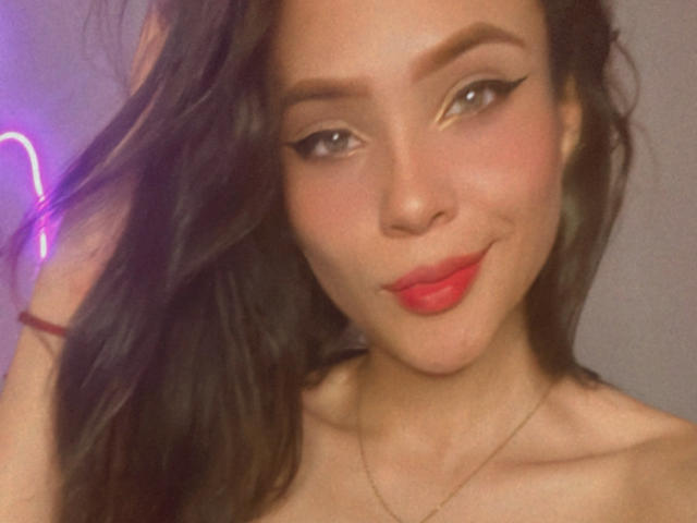 Lara Mancini ha i capelli scuri e ondulati, rossetto rosso e eyeliner applicato ad "ala di gabbiano". Sorride con un'espressione carina e sicura di sé, indossa una sottile collana e si tocca i capelli..