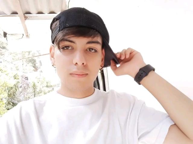 TheShiningMen with a black mesh cap, white t-shirt, and black wristwatch, holding a phone to their ear, has short brown hair, a nose ring, and a slight smile.