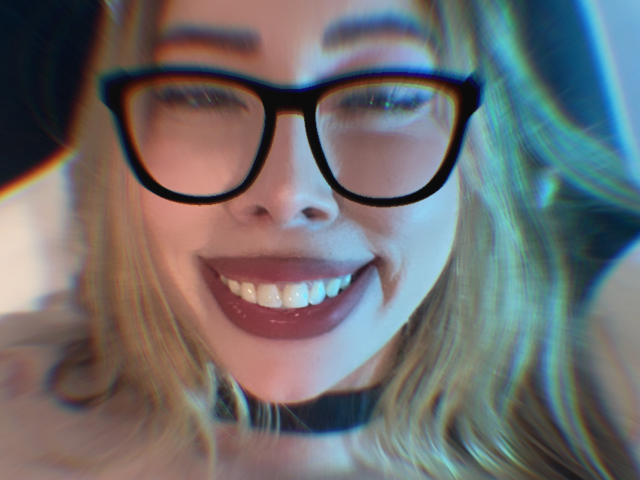 Het gezicht van JennyLawry, met een glimlach en donkerrode lippenstift, draagt zwarte brillen en een zwarte choker, blond haar, vage achtergrond, subtiel blauw-groen filtereffect, waarbij haar tanden zichtbaar zijn..