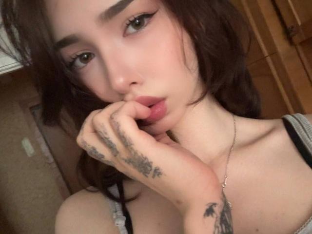 KeilaJavellana with pouty lips, brown eyes, and dark wavy hair, touching her slightly open mouth with tattooed hand, wearing a black and white top.