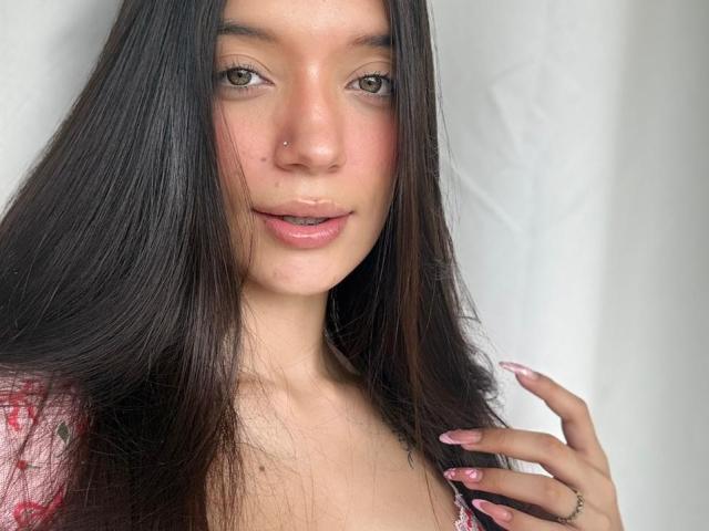 Michell Ford tiene el pelo largo y oscuro, ojos verdes, un piercing en la nariz, labios rosados y piel clara. Sus uñas rosadas rozan su cabello, mostrando un anillo. No se ven sus senos..