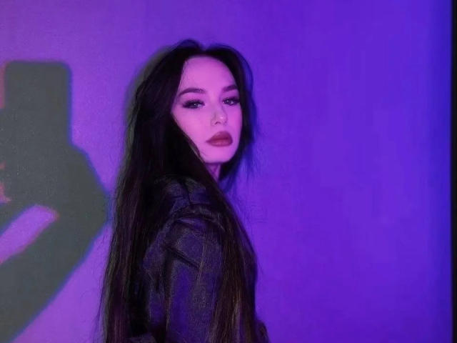 ChaneCarco with long dark hair, wearing a black leather jacket, looking over her shoulder with a serious expression, purple lighting, and a shadow on the left.