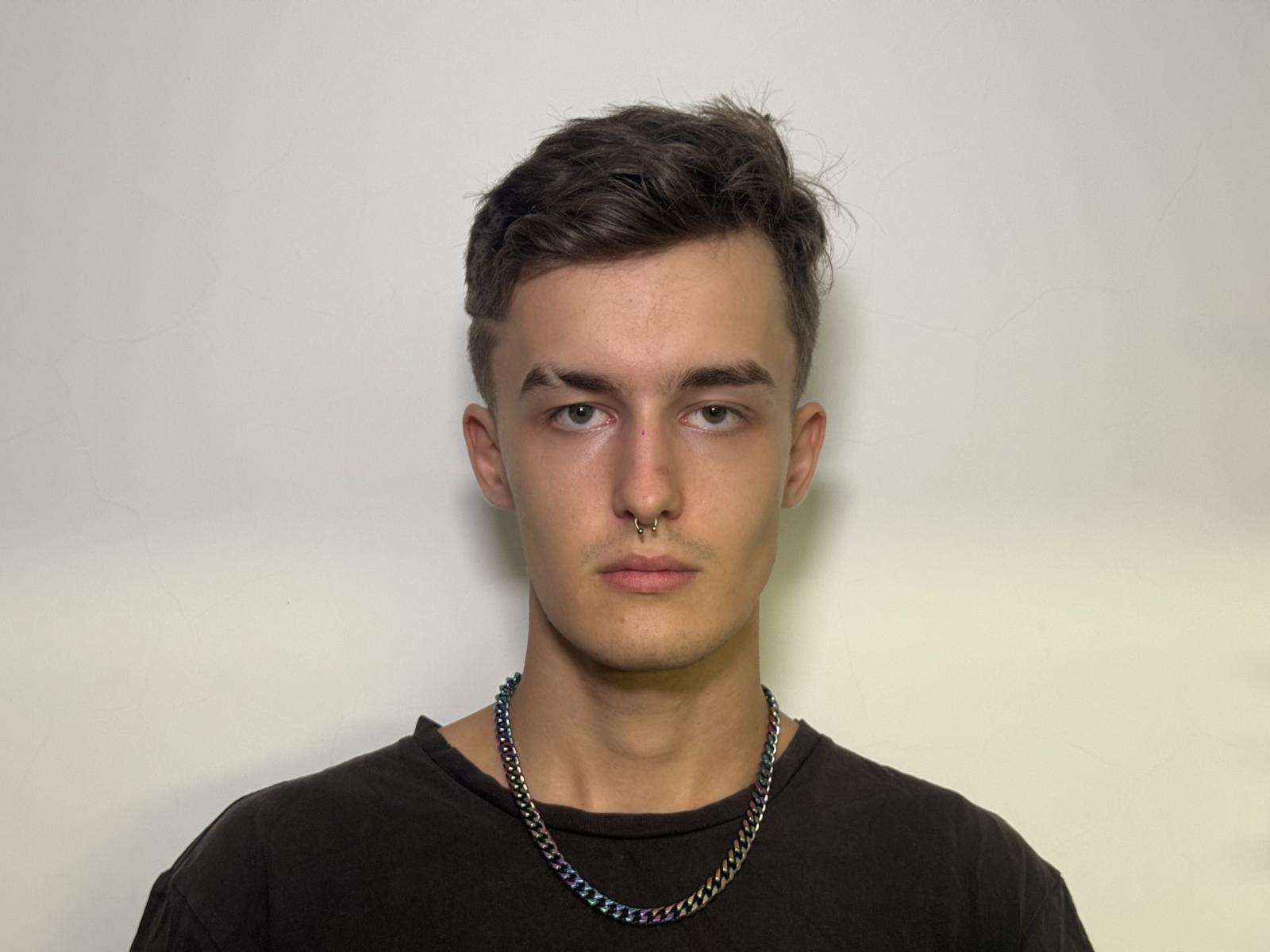 Manuel Landquist, met kort, donkerbruin haar, een neusring en een ketting, draagt een zwart shirt en heeft een serieuze blik..