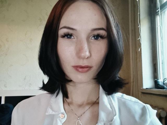 Nathalie Dutt, con i capelli neri corti, gli occhi azzurri e le lentiggini, indossa una camicia bianca con bottoni ed ha una collana con un piccolo ciondolo circolare, guardando direttamente verso la fotocamera..
