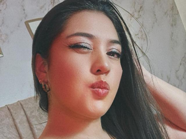 PaulaAnd has puffy red lips, dark straight hair, and wears gold hoop earrings. Her eyes are half-closed with thick black eyeliner. She's making a pouty face.