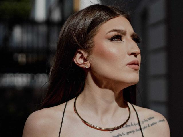 Tesakelle tem cabelos castanhos e brilhantes, cílios longos e um rosto radiante. Ela está vestindo uma blusa preta de alças e uma pequena tatuagem é visível em seu ombro direito..