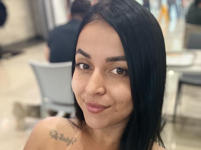 HikariChloe has medium brown skin, black straight hair, brown eyes, and a small smile. She has a tattoo on her left shoulder and is topless.