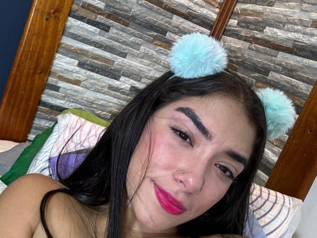 SharonKlart has black hair, blue fluffy cat ears, pink lipstick, a nose ring, and a slight smile, with her tits partially visible in the bottom left corner.