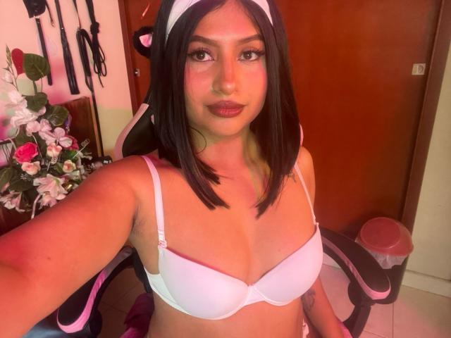 ZarayWhitMoreLove has medium tits, wearing a white bra and cat ears, with black hair and a white headband, sitting in a chair, holding a selfie.
