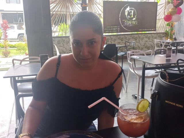 DamaraFoxy with dark hair in an off-shoulder black top, sitting at a table with a drink, pink straw, lemon slice, and bag labeled "MONT BLANC".