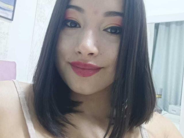 AlexaLaker a les cheveux brun foncé, mi-longs, avec du fard à paupières rose, de l'eye-liner noir et du rouge à lèvres rouge. Elle sourit, et on peut apercevoir ses seins de taille moyenne sous un débardeur blanc..