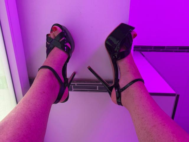 Cindy-Stone1-hot's benen, gekleed in zwarte sandalen met hoge hakken en bandjes, met naar boven wijzende tenen, huid met sproeten, paars en roze verlichting..