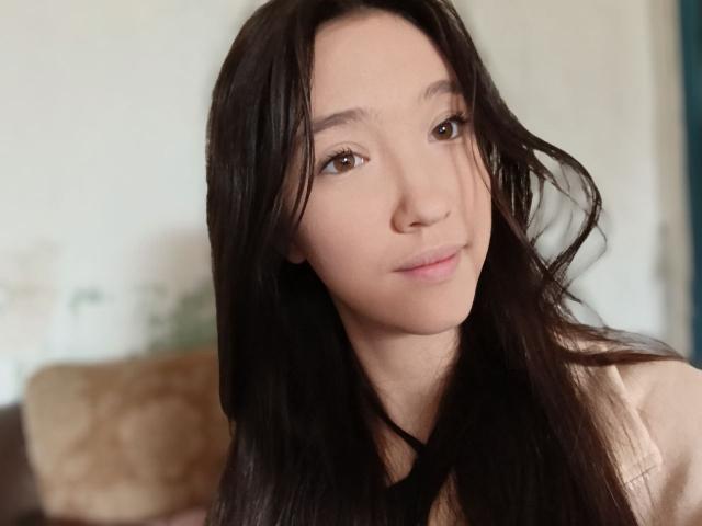 AshleyNaone tiene el cabello largo y castaño oscuro, piel clara, ojos marrones y una sonrisa sutil. Lleva una blusa color beige y está mirando ligeramente hacia un lado..