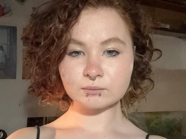 Catherine Eccles ha i capelli castano ricci, la pelle chiara, gli occhi azzurri, un anello al naso e un piercing al labbro inferiore. Indossa un top nero con spalline, ha un'espressione seria e un leggero rossore sul viso..
