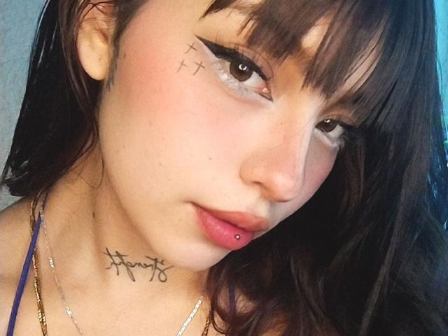 KuroBabee has dark brown eyes, black eyeliner with sharp wings, a lip piercing, and a tattoo under her chin. She has a small cross tattoo on her right cheek.