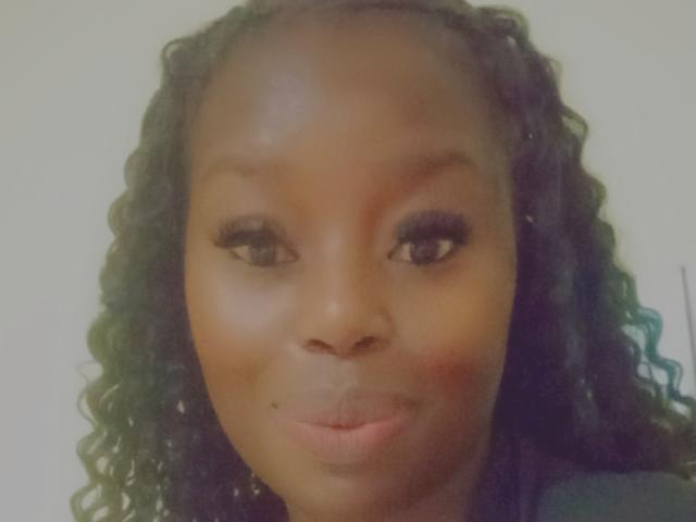 BlackBeryHottie with dark brown skin, curly black hair, and a subtle smile, has long eyelashes, a small beauty mark below her right eye, and slightly flushed cheeks.