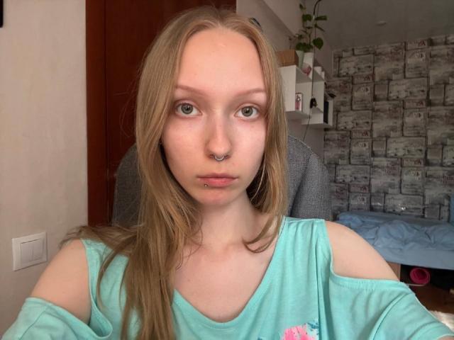 RendaPancake tem pele clara, olhos verdes e cabelos longos e loiros. Ela está vestindo uma blusa turquesa com um ombro de fora, com uma flor rosa, um piercing no nariz e um piercing no lábio..
