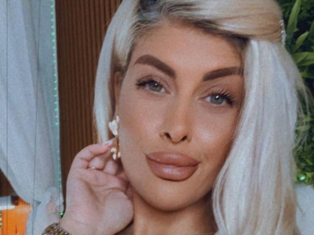 SalmaRoze met blond haar, dikke wenkbrauwen, volle roze lippen en een schattige, kleine neus, die haar oor aanraakt met een hand met een ring. Ze kijkt naar de camera..