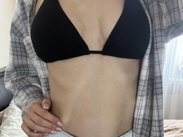 Valnes portant un soutien-gorge noir, exposant ses seins, avec une chemise à carreaux ouverte, une main sur sa hanche, montrant son ventre plat et sa peau pâle..