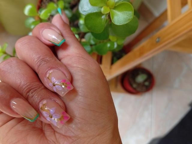 LailaCastillo's hand with glossy, nude-pink nails featuring colorful, floral accents and gold embellishments, showing off her neatly manicured, feminine nails. Her skin is a warm, medium tone.