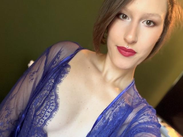 JadeFrenchKiss with red lipstick, blue lace top, showing her tits, small nose ring, light skin, brown hair, and green eyes, looking at the camera, smiling.
