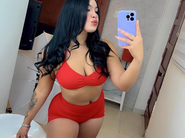 MiaDenver with long black hair, wearing a red bra and red shorts, taking a mirror selfie with a purple phone, showing her large tits and curvy ass.