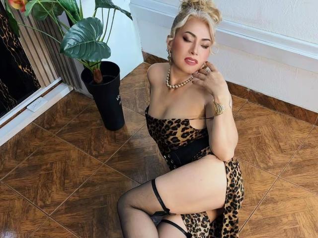 MisseScarleth has blonde hair in a bun, wearing a leopard print dress, black garter, and stockings, with a pearl necklace, sitting on a wooden floor, showing her ass.