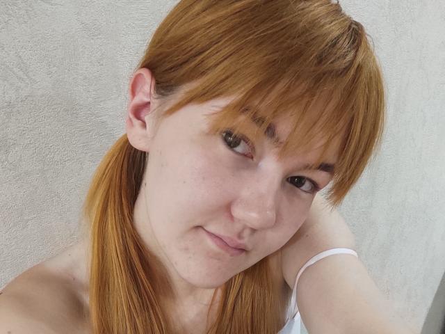 SheritaChieng tiene el cabello castaño claro, pecas y una ligera sonrisa. Lleva una correa blanca, y sus ojos marrones miran hacia un lado. Su nariz es pequeña, y tiene la piel clara..