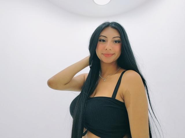 MadissonStar, con cabello negro largo, vistiendo un top corto negro con textura, mostrando sus pechos, sonriendo, con la mano en el cabello, fondo blanco, linda, asiática, piel clara, collar..