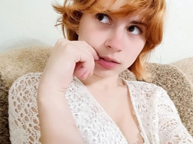 MireilleSpotwood with short red hair, pale skin, and pouty lips, wearing a white lace top, biting her finger, looking up with big brown eyes, soft pink lips.