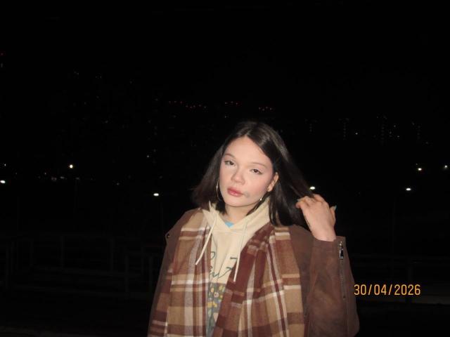 Tawana Shillinger, com cabelo preto liso, pele clara, vestindo um cachecol xadrez marrom e um casaco marrom, segurando o cabelo com a mão direita, durante a noite, com data e hora. 30/04/2006.