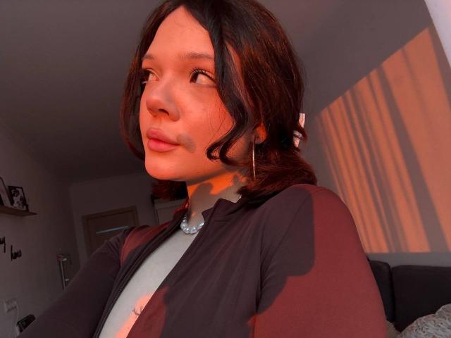 Tawana Shillinger, con piel de color marrón medio, cabello ondulado de color marrón oscuro y senos pequeños, vestida con una camisa negra y roja, un collar de perlas y aros grandes, bajo la luz cálida del sol..