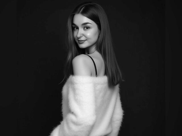 SmileForMee with long straight hair, wearing a fluffy white off-shoulder top, showing a cute smile and looking over her shoulder. Black and white, boobs slightly visible.