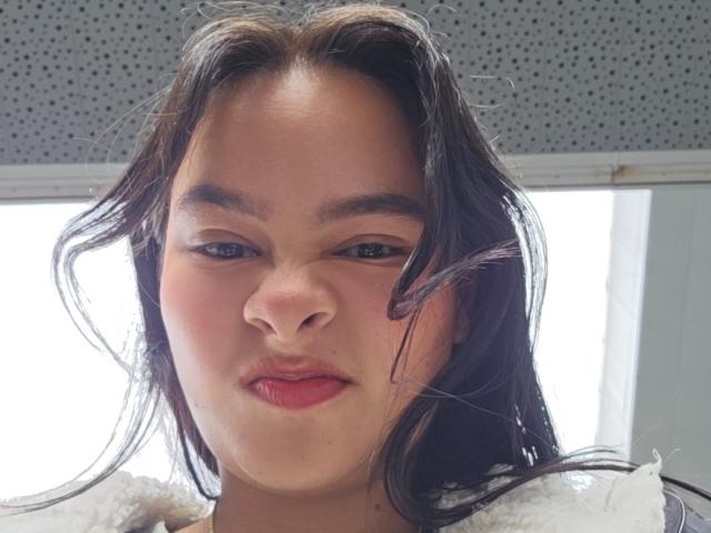 Yurimy heeft volle, rode lippen, lichtrode wangen en donkerbruin, golvend haar dat naar de zijkant waait. Haar bruine ogen zijn half open, en ze draagt een witte top..