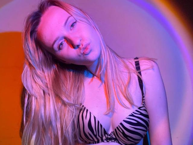 FlyFreedom, con i capelli biondi, le labbra carnose e un reggiseno a stampa zebrata, mostra il suo seno illuminato da luci rosa e blu..