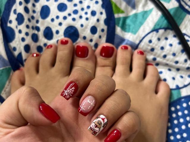 SharonKlart's red-painted toes with glossy nail polish, one nail featuring a snowflake and another with a cute cartoon face, resting on a blue and white patterned quilt.