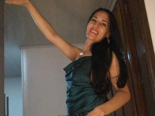 MiaMott tiene el pelo largo y negro, una sonrisa, y lleva un vestido verde sin tirantes con un colgante blanco, levantando un brazo. Sus pechos son pequeños, y es atractiva..