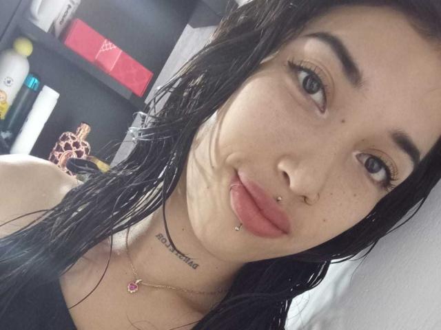 Krystal Evans, com cabelo preto molhado, pele clara, nariz e lábio inferior perfurados, olhos azuis e uma tatuagem abaixo do queixo. Ela está usando um colar com uma pedra rosa..
