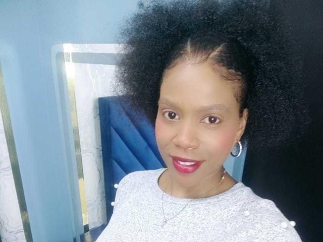 SarahiPusey has a big, fluffy black Afro, brown eyes, red lipstick, gray textured top, and hoop earrings. She's wearing a nose ring and a delicate necklace.