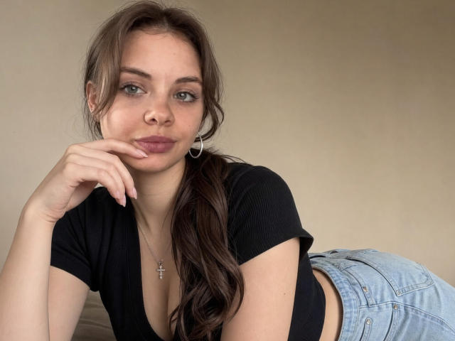 Lilia Pochatko, con le labbra piene, i capelli castani raccolti in una coda di cavallo, indossa un top corto nero, jeans blu e una croce. È sdraiata, con una mano sul mento, e porta degli orecchini a cerchio..