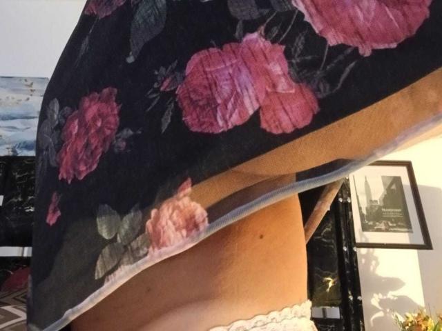 La gonna floreale di ZarayFeet viene sollevata, rivelando biancheria intima in pizzo bianco e un'occhiata al suo sedere abbronzato e liscio. Un tessuto trasparente mostra rose rosa su uno sfondo scuro..