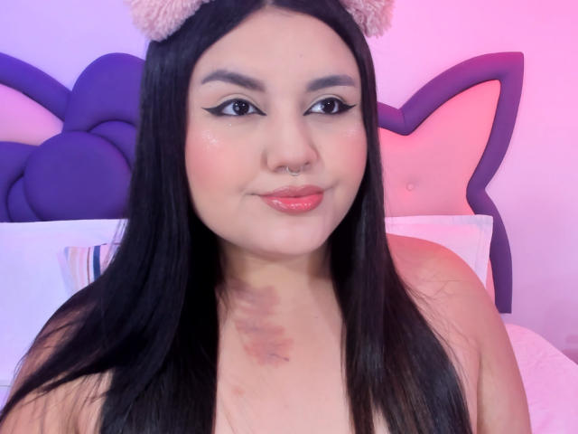 MarlaBriard has black hair, cute cat ears, and a nose ring. She's smiling with pink lips, wearing eyeliner, and has a bruise on her chest. She's topless.