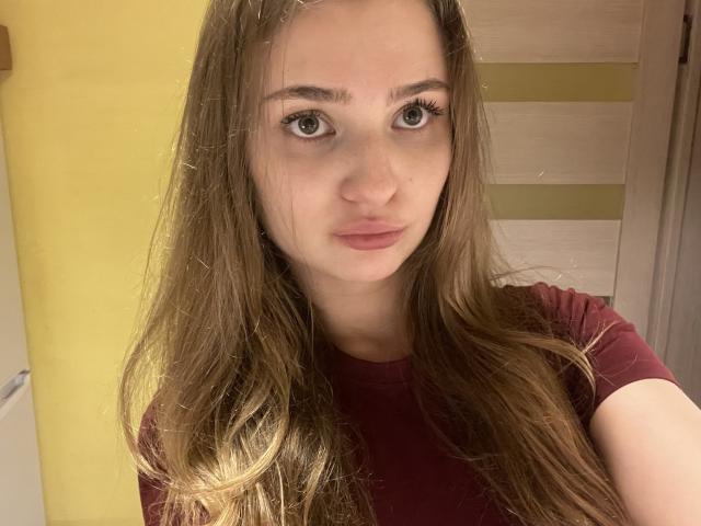 Lesia Bengtson, avec ses longs cheveux bruns, ses yeux verts et ses lèvres roses légèrement retroussées, porte une chemise rouge sur cette photo d'elle-même. Ses seins ne sont pas visibles, on ne voit que son visage..