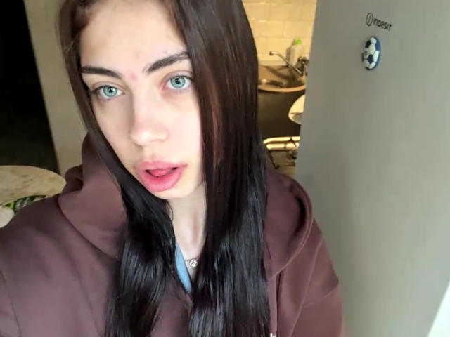 AureaVandale hat langes, braunes Haar, blaue Augen und trägt eine braune Kapuzenjacke. Ihr Mund ist leicht geöffnet. Sie hat eine kleine, rote Markierung auf ihrer rechten Wange..
