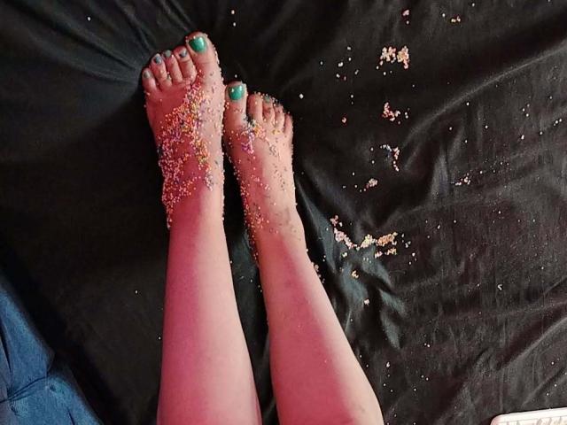 StephanieSun's sandy-assed feet with green-painted toes, covered in small pebbles, lying on a black sheet. Her toes are slightly spread, showing some pebbles stuck to her skin.
