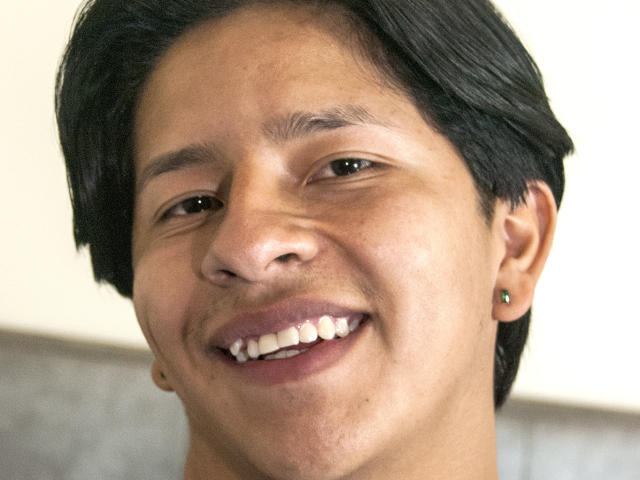 VictumMontenegro tem cabelo preto e liso, olhos castanhos e um sorriso discreto, com os dentes visíveis. Ele está usando pequenas brincos e tem um tom de pele bronzeado..
