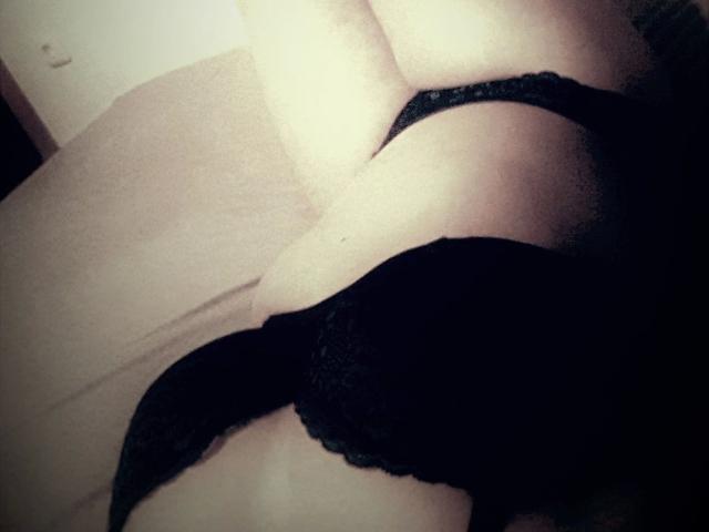 Il reggiseno di pizzo nero di TessaRubin-hot aderisce al seno, la sua pelle chiara contrasta con il tessuto scuro, il suo braccio destro è sollevato, poggiato su una superficie beige..