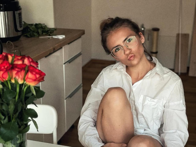 HelenRosy con gli occhiali, labbra tumefatte, camicia bianca, ginocchio sollevato, seduta vicino a rose rosse, bancone da cucina in legno, microonde sullo sfondo, che guarda la fotocamera, carina, luce soffusa..